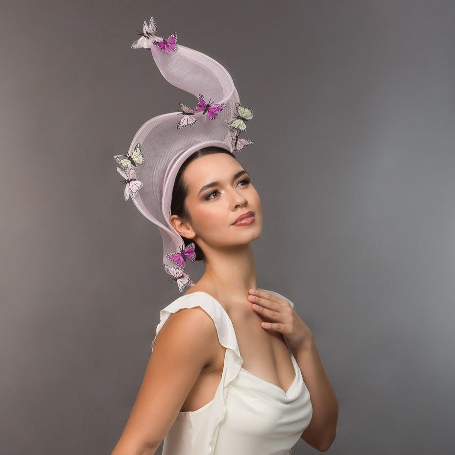 A model wearing a decorative pale pink crinoline headpiece with butterflies against a gray background